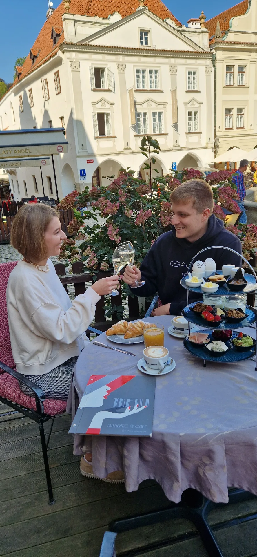 A couple toasting with sparkling wine over breakfast on the Authentic Café terrace